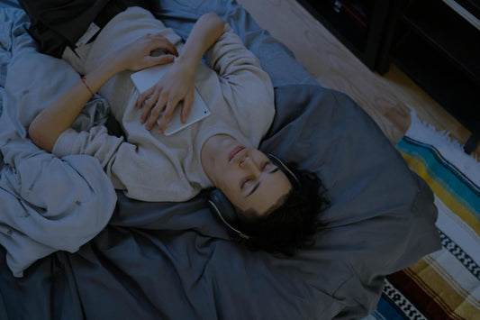 Personne allongée dans un lit, casque audio sur les oreilles, profitant d’un moment de calme propice au sommeil grâce au bruit blanc